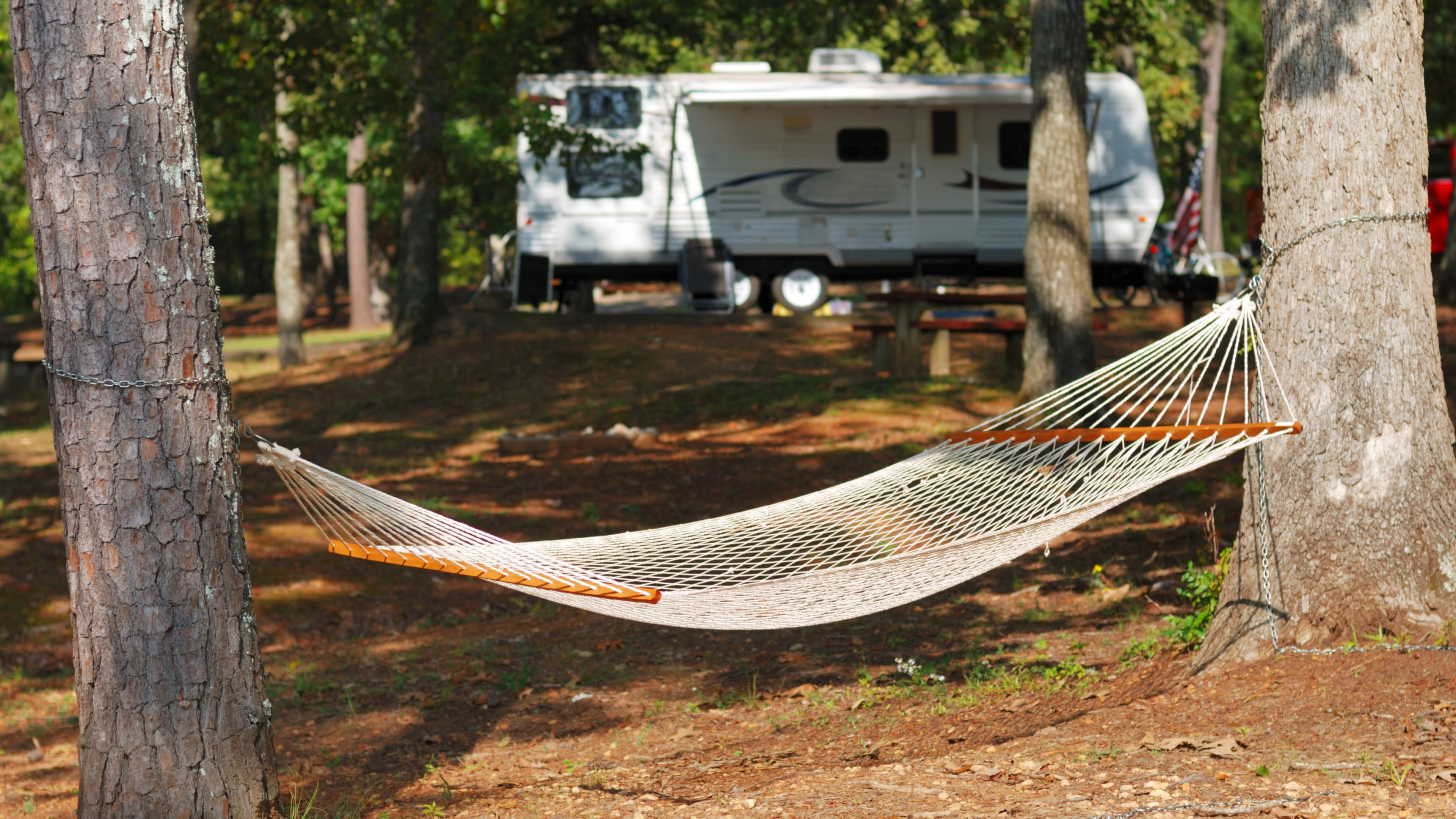 A camping hammock strung between two trees with a tarp overhead in the forest