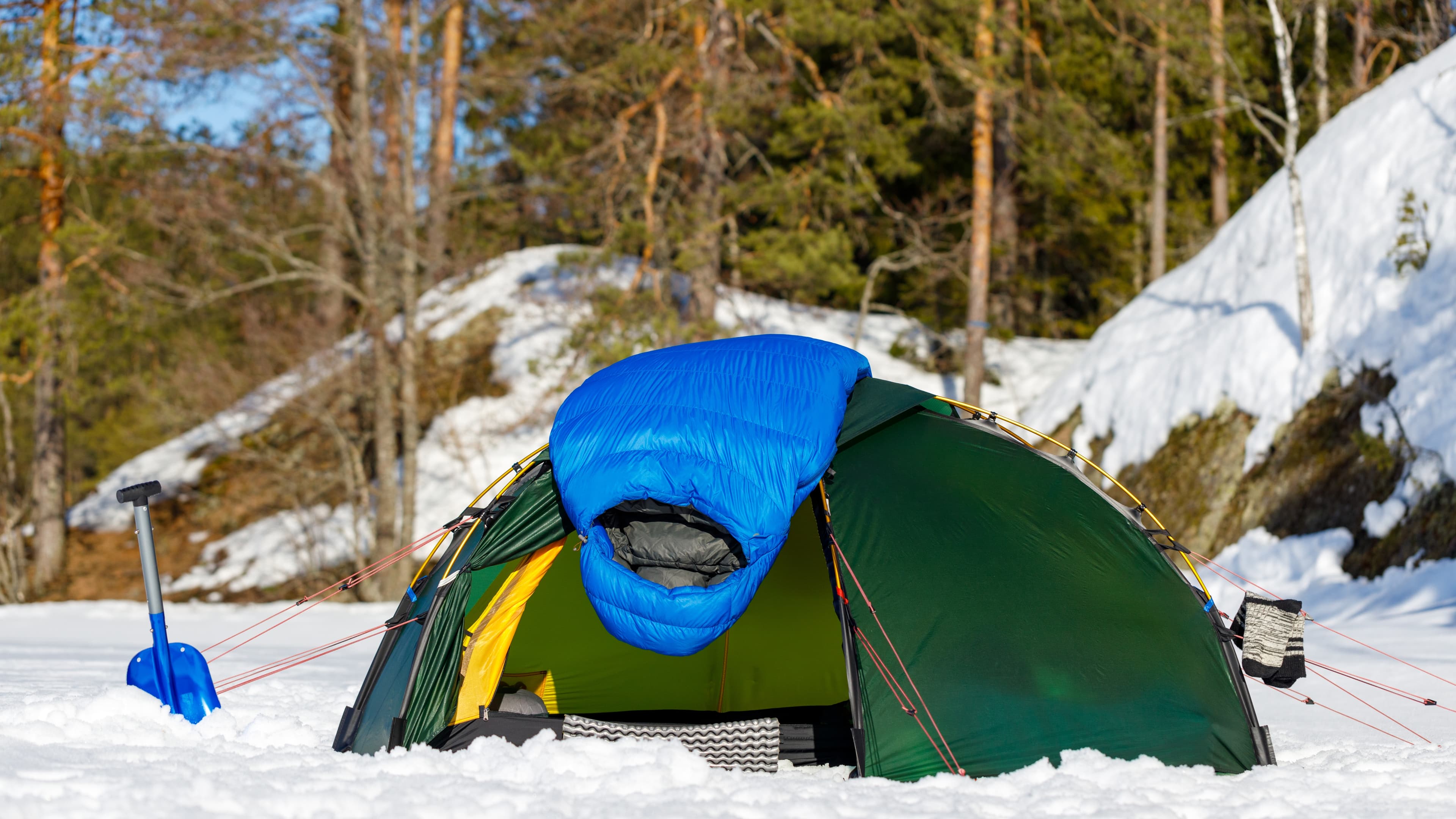 A tent glowing with lantern light in a snow-covered winter campsite at dusk