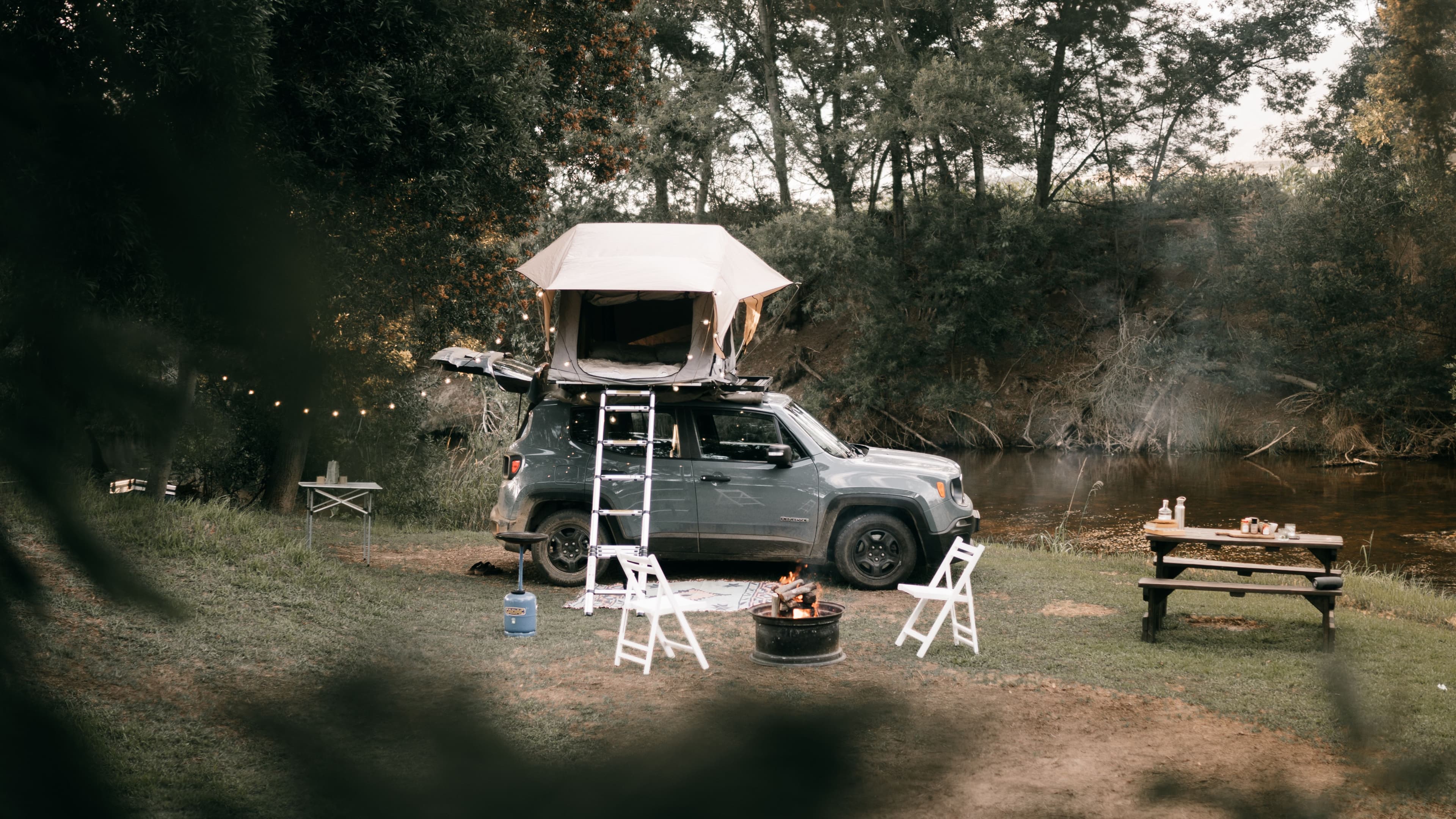 A tent and camp chairs set up beside a parked vehicle at a campsite